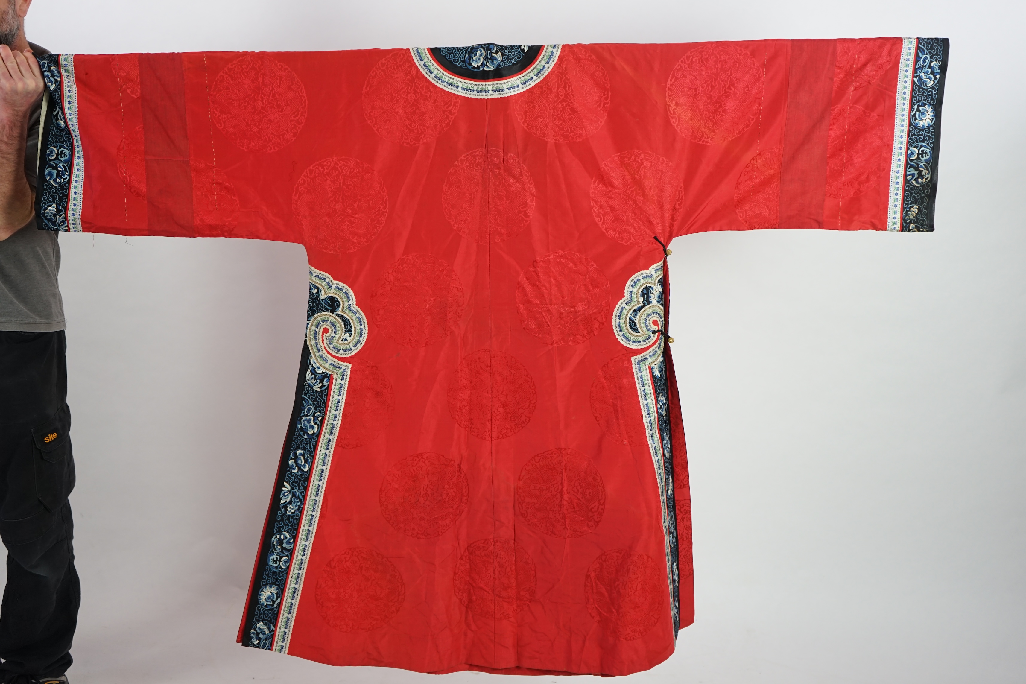 A late 19th century Chinese Manchu ladies red silk damask robe, with black and blue silk embroidered borders, ornately edged cream floral silk braiding, length from neck (back) to bottom edge 132cm long. Condition - stai